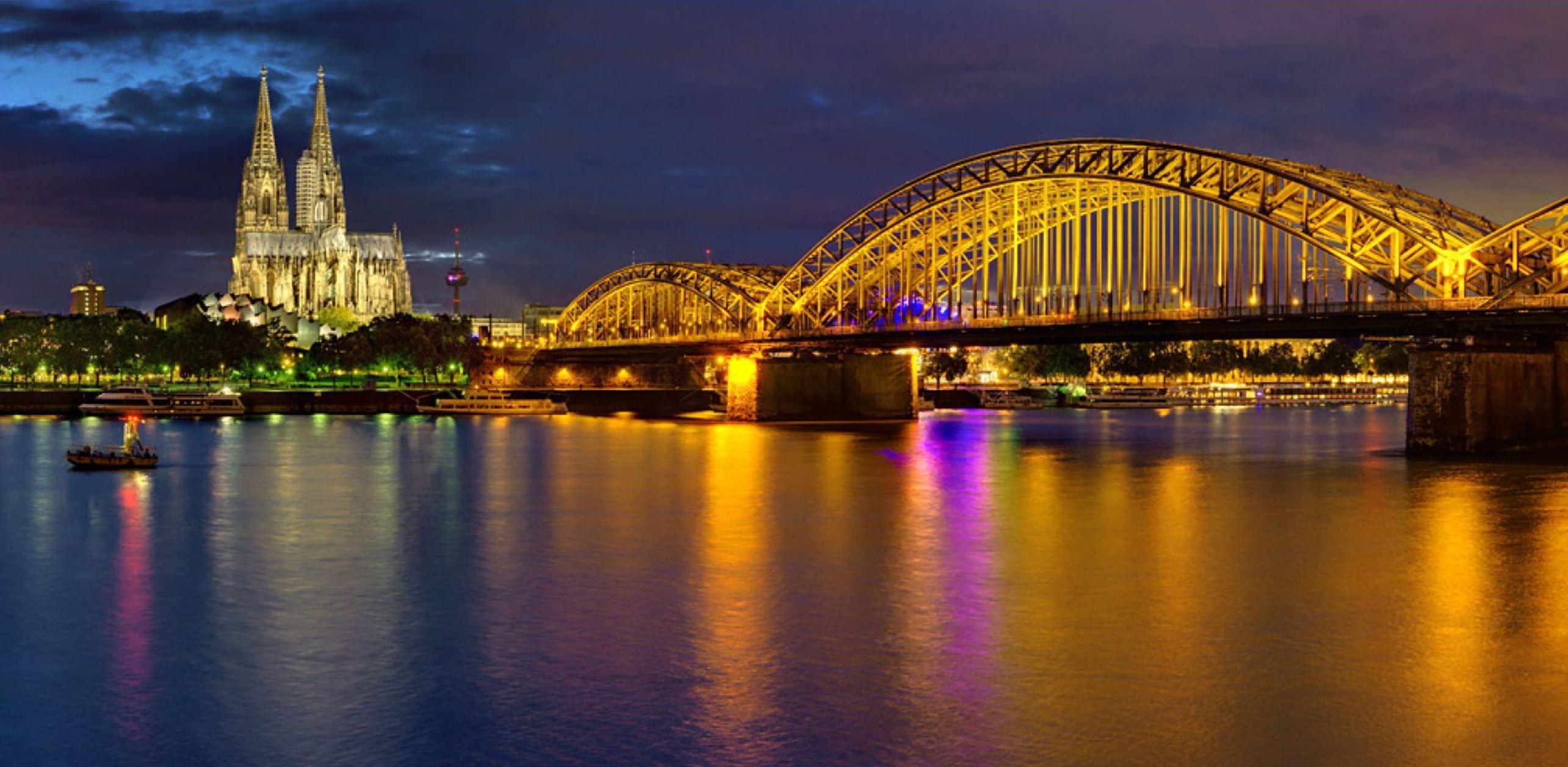 Kölner Dom und Hohenzollernbrücke bei Nacht, die Lichter spiegeln sich im Rhein